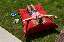 Load image into Gallery viewer, Girl Laying on a Red Fatboy Original Slim Outdoor Bean Bag in the Grass
