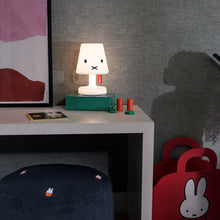 Load image into Gallery viewer, Desk with a small lamp, books, and a dark blue ottoman with embroidered designs in a room.
