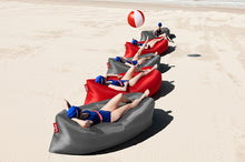 Load image into Gallery viewer, Girls Laying on Steel Grey and Red Fatboy Lamzac Version 3.0 Inflatable Loungers on the Beach
