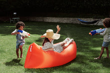 Load image into Gallery viewer, Lady Laying on a Tulip Orange Fatboy Lamzac Version 3.0 Inflatable Lounger Getting Squirted by Water Guns
