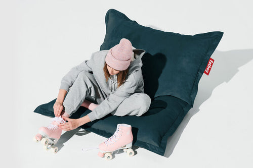 Person sitting on a large dark blue pillow wearing pink roller skates and a pink beanie.