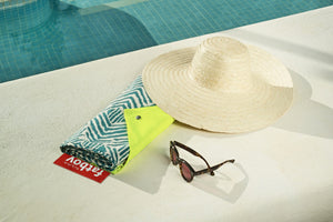 Bali Fatboy Miasun Sun Shade Folded on a Pool Deck Next to a Hat and Sunglasses