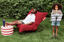 Load image into Gallery viewer, Guy Sitting on a Red Fatboy Original Slim Outdoor Bean Bag Rocker in the Grass
