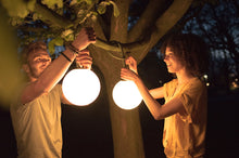 Load image into Gallery viewer, Guy and Girl Hanging Fatboy Bolleke Lamps from a Tree Branch at Night

