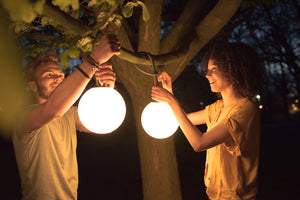 Guy and Girl Hanging Fatboy Bolleke Lamps from a Tree Branch at Night