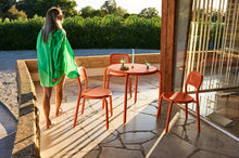 Load image into Gallery viewer, Model Walking by a Tangerine Fatboy Toni Bistreau Table and Chairs on a Patio
